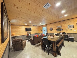 Ein Zimmer mit Holzwänden, einem Fernseher, einem Kamin, einer Uhr und einem Esstisch mit Stühlen.