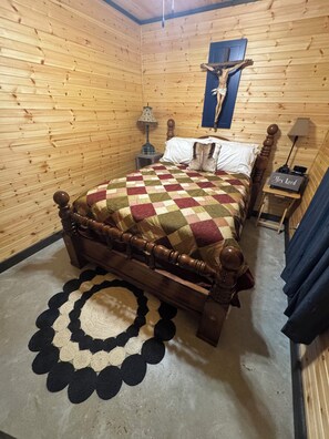 A wooden-paneled room with a bed, a crucifix on the wall, a small table with a lamp, and a rug. - SIMPLY BLESSED ON LANAN BAY (Many)
