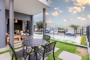 Eine Terrasse mit rundem Tisch und Stühlen, ein Schwimmbecken und der Blick auf geparkte Autos und Gebäude.