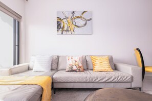 Ein modernes Wohnzimmer mit einer Couch, zwei Kissen, einem gelben Sessel und einem an der Wand befestigten abstrakten Gemälde.