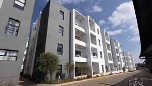 Un immeuble résidentiel moderne à plusieurs étages, doté de balcons, d’une allée pavée et surplombant un ciel dégagé.