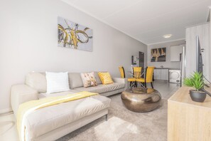 Ein modernes Wohnzimmer mit einer Couch, einem Couchtisch und Sesseln. Im Hintergrund ist eine Küchenzeile zu sehen.