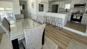 Una cocina moderna con comedor, que incluye una mesa de vidrio, sillas de mimbre y piso de madera.