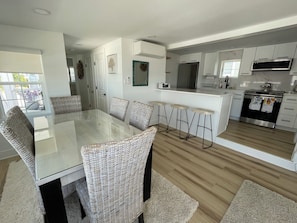 Una cocina moderna con comedor, que incluye una mesa de vidrio, sillas de mimbre y piso de madera.