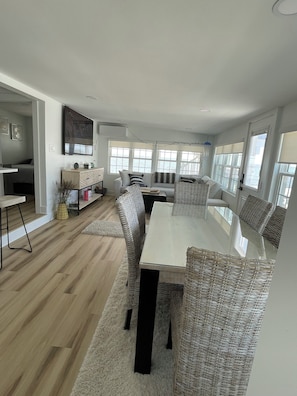 A modern living room with a glass-top dining table, wicker chairs, a sofa, and a large window overlooking the sea. - This spectacular home marries BEACHfront and BAYfront! (Cape May Court house)