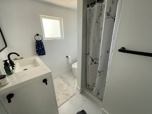 Une salle de bain équipée d’un lavabo, de toilettes, d’un rideau de douche et d’une fenêtre.