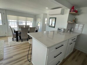 A modern kitchen with white cabinetry, a built-in island, and a dining area with wicker chairs. - This spectacular home marries BEACHfront and BAYfront! (Cape May Court house)