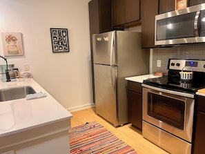 Una cocina moderna con electrodomésticos de acero inoxidable, una encimera blanca y una alfombra colorida.