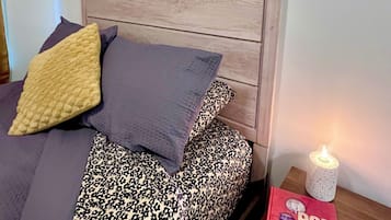 A bedroom with a bed, pillows, a bedside table with a book and a candle, and two framed pictures on the wall.