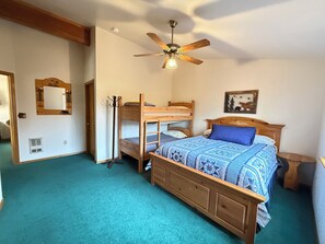 Ein Zimmer mit Etagenbetten, Deckenventilator, Holz-Kopfschild, gerahmtem Bild und kleinem Tisch.
