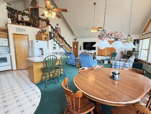 Eine geräumige Küche mit Essbereich, Holzstühlen, einem runden Tisch und einer Treppe, die zu einem Schlafzimmer auf dem Dach führt.
