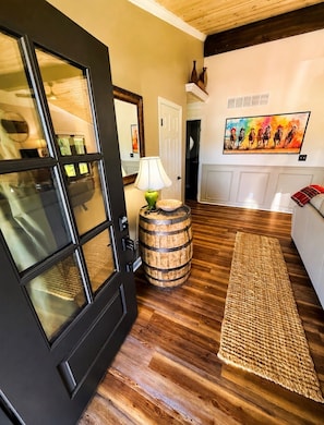 A room with a wooden floor, a black door, a lamp, a barrel, a woven rug, and a painting on the wall. - Bourbon Trail Lodge, Kentucky Derby, close to Louisville, Bardstown! (Mount Washington)
