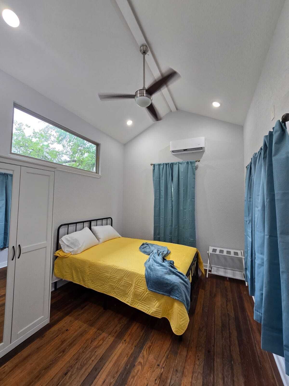 A room with a bed, a ceiling fan, an air conditioning unit, and a window.