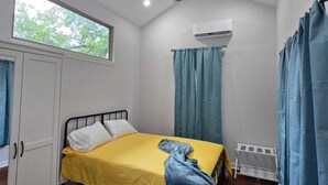 Ein Zimmer mit einem Bett, einem Deckenventilator, einer Klimaanlage und einem Fenster.