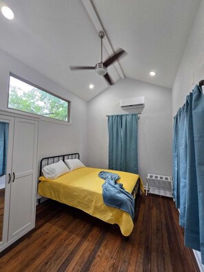 A room with a bed, a ceiling fan, an air conditioning unit, and a window. - Casita 2 minutes from the Alamodome (San Antonio)