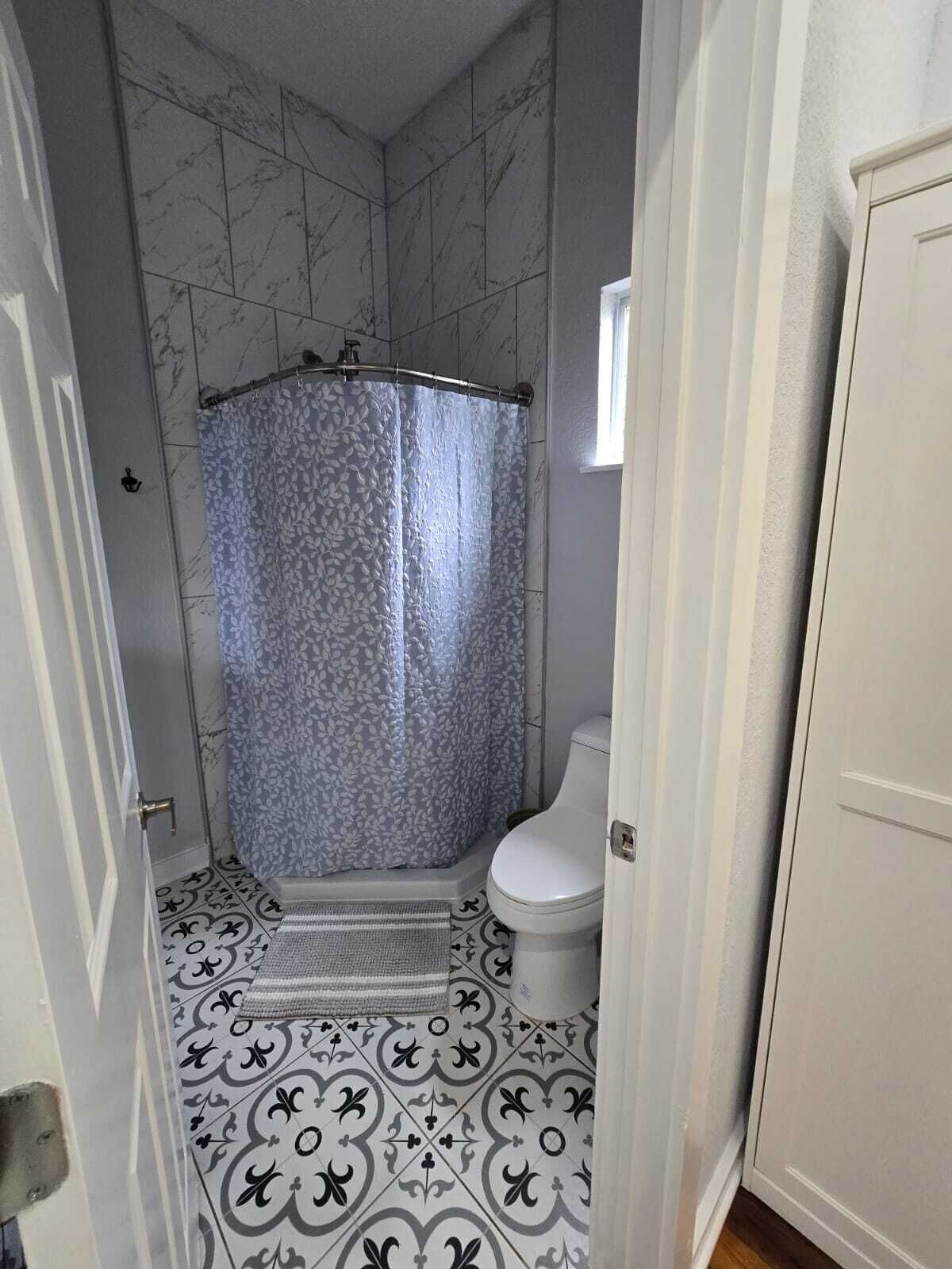 A bathroom with a shower, toilet, and patterned floor tiles.