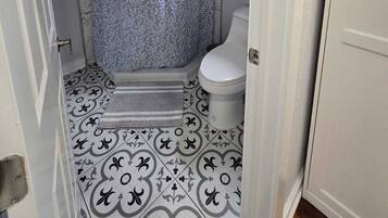 A bathroom with a shower, toilet, and patterned floor tiles.