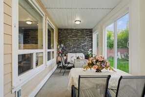 Eine überdachte Terrasse mit Steinmauer, einem Tisch und Stühlen sowie Blick auf den Garten.
