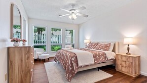 A bedroom with a bed, bedside tables, a desk, a chair, a mirror, and a ceiling fan.