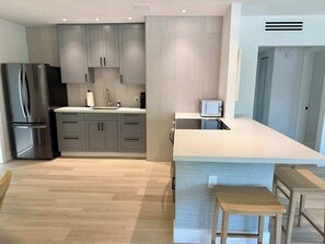 Eine moderne Küche mit grauen Schränken, einem Edelstahlkühlschrank, einer Mikrowelle und einem kleinen Holztisch.