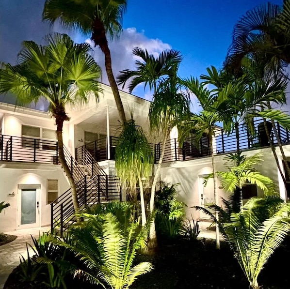 A multi-story building with a central staircase, surrounded by palm trees and lush greenery.