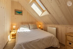 A cozy attic bedroom with a sloped ceiling, a skylight, a bed with white bedding, two bedside tables with lamps, and a painting on the wall. - La Correrie des Chartreux (AILLON LE JEUNE)