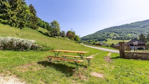 A picnic table in a grassy area with a road and buildings in the background. - La Correrie des Chartreux (AILLON LE JEUNE)