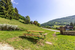Ein Picknicktisch in einer grünen Wiese, im Hintergrund eine Straße und Gebäude.