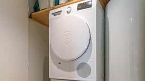 A compact laundry room with stacked appliances, including a dryer and a washing machine, and a water heater. - La Correrie des Chartreux (AILLON LE JEUNE)