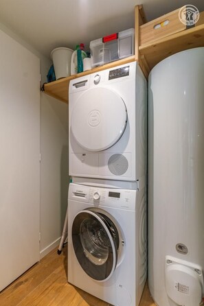 Ein kleinerer Waschraum mit übereinander gestapelten Geräten, darunter ein Trockner und eine Waschmaschine, sowie ein Warmwasserbereiter.