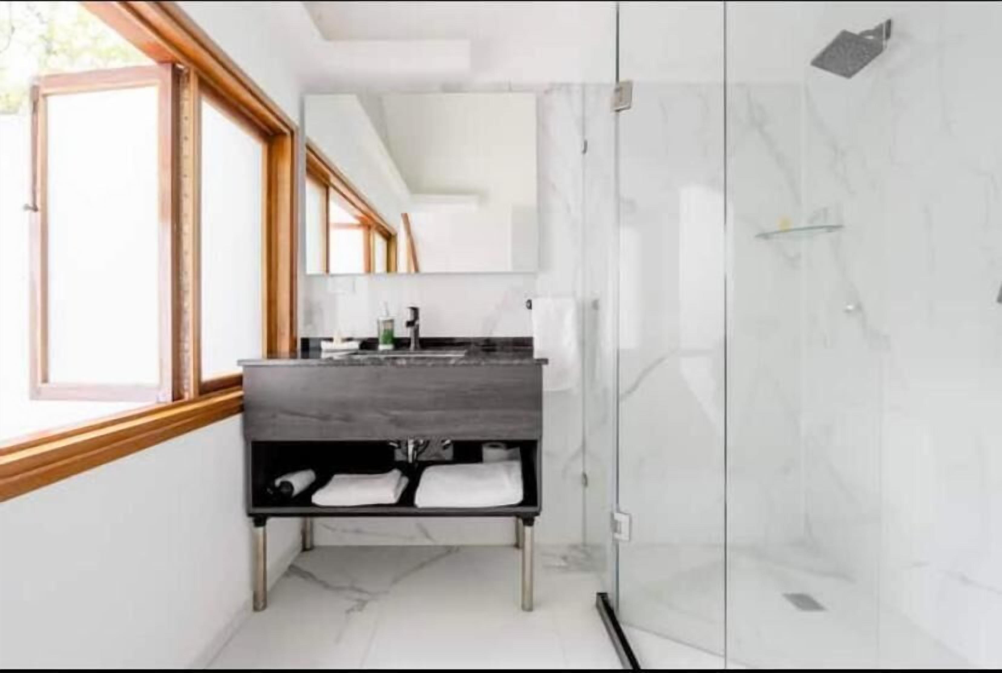 A modern bathroom with a glass shower enclosure, a wooden-framed window, and a dark countertop.