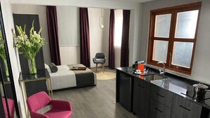 Habitación de hotel compacta con cama, pequeña mesa de comedor, una silla, zona de cocina y un ventanal amplio.