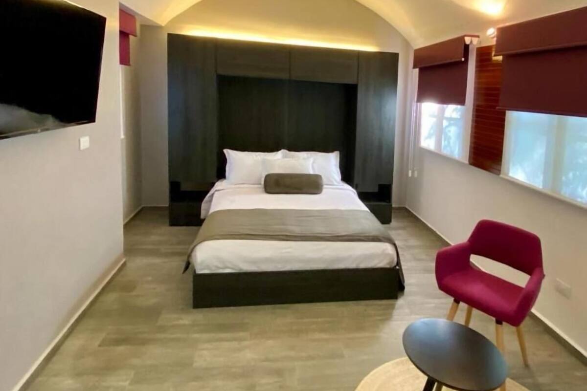 A bedroom with a bed, a chair, a television, and a window.