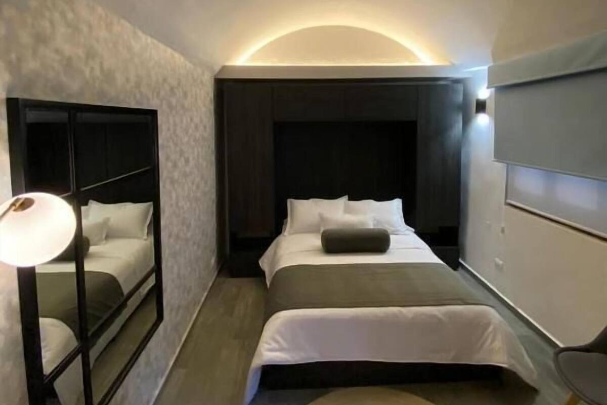 A modern hotel room with a curved ceiling, a large bed, a bedside table, and a mirror.