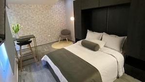 Una habitación de hotel moderna con cama, mesita de noche y un pequeño rincón de descanso.