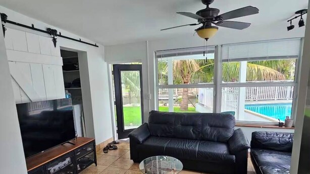 A living room with a TV, leather sofa, ottoman, ceiling fan, and a view of a swimming pool. - Waterfront~Boat Deck, Pool home near Hard Rock~FLL Airport & FIFA World Cup (Fort Lauderdale)