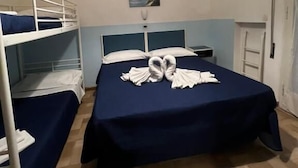 Une chambre avec des lits superposés, un lit décoré avec une serviette en forme de cygne, une lampe fixée au mur et une porte.