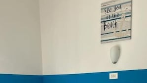 Un lit avec une literie blanche et bleue, une serviette pliée, une table de chevet et un panneau décoratif au mur.