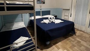 Une chambre avec des lits superposés, un lit simple, une fenêtre avec des rideaux et un luminaire fixé au mur.