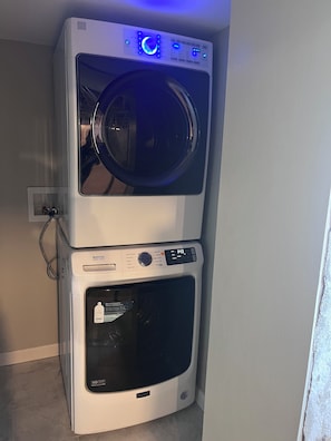 Lavadora y secadora apiladas con un panel de control que muestra la hora y las configuraciones.