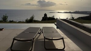 An outdoor seating area with lounge chairs facing a sunset view over a body of water. - Modern Pelican St. Maarten Escape with Pool, Views & Outdoor Lounge (Cole Bay)
