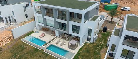 A modern two-story building with a rooftop pool, outdoor seating, and a landscaped yard.