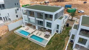 A modern two-story building with a rooftop pool, outdoor seating, and a landscaped yard. - Modern Pelican St. Maarten Escape with Pool, Views & Outdoor Lounge (Cole Bay)