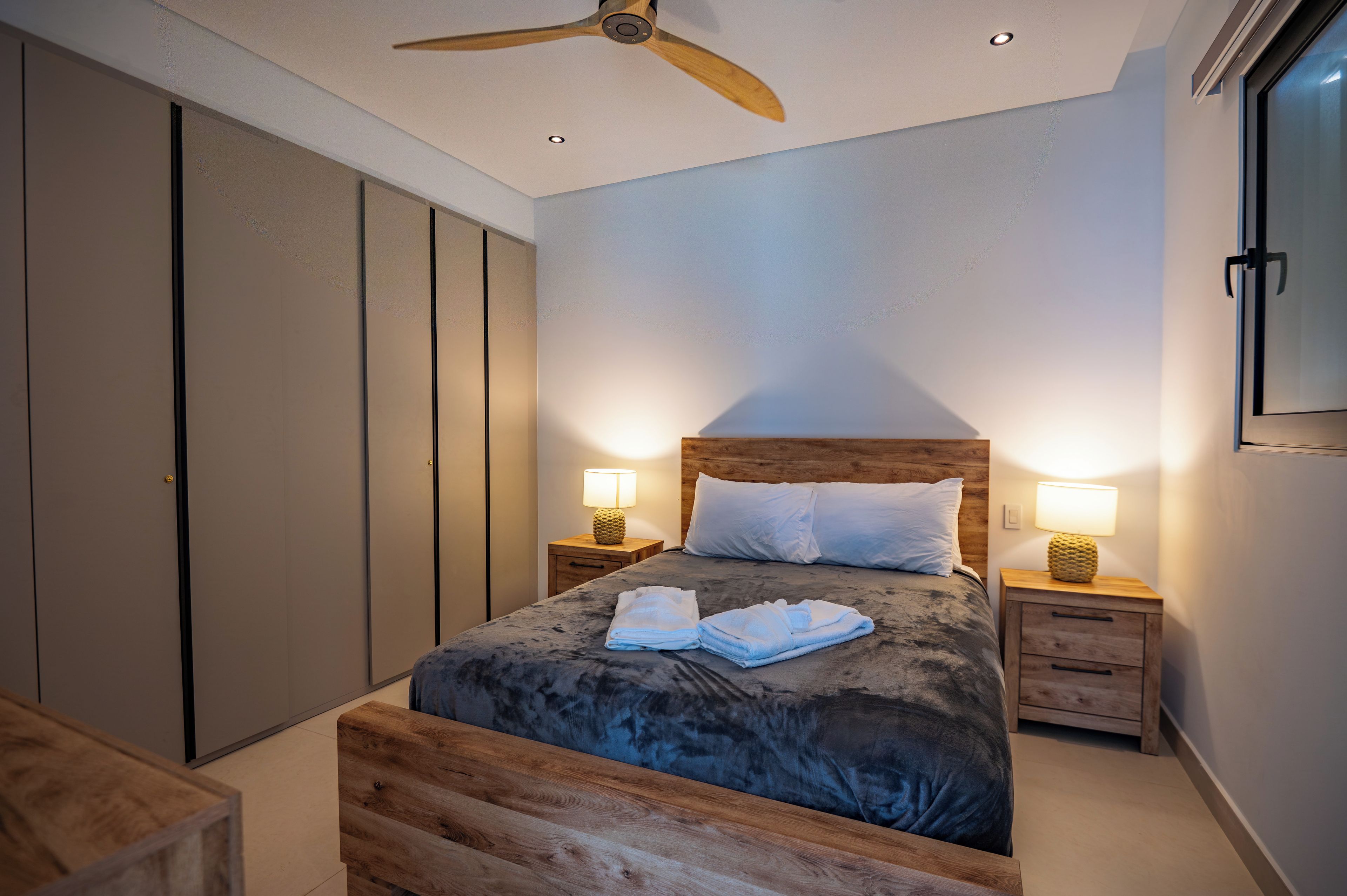 Un dormitorio con una cama, dos lámparas de noche, un ventilador de techo y un cabecero de madera.