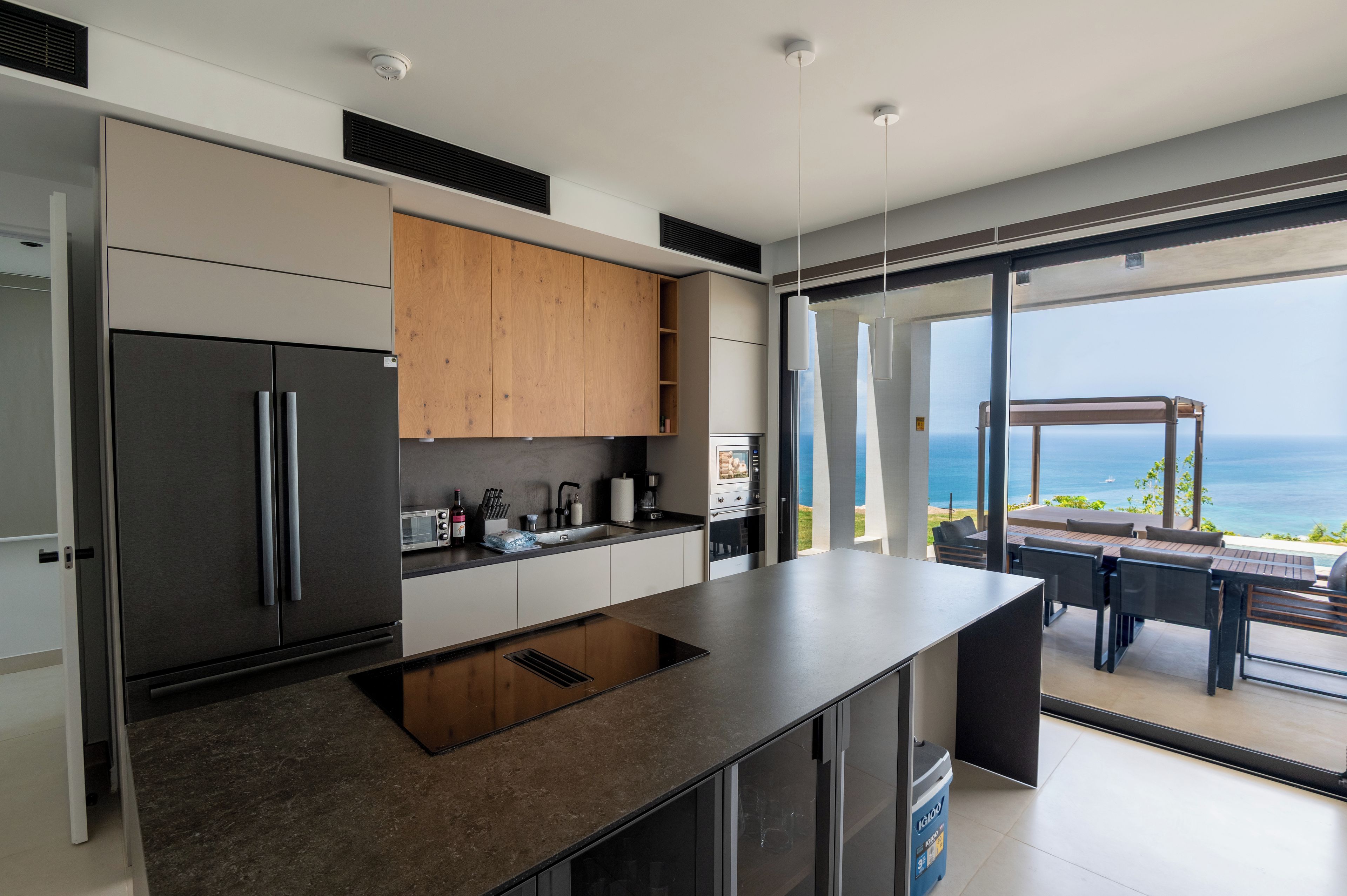 A modern kitchen with a built-in island, stainless steel appliances, and a view of the ocean through large sliding glass doors.