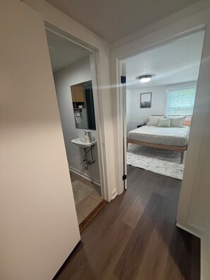 A bedroom with a bed, a nightstand, a window with blinds, and a bathroom with a sink and mirror. - Private Saratoga retreat - Travel Nurses, Business professionals, Professors (Gansevoort)