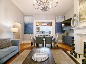 A dining area with a chandelier, a fireplace, and a kitchen in the background. - Spacious Historic 2BR w/ Courtyard, Parking, Walk to Forsyth Park (Savannah)