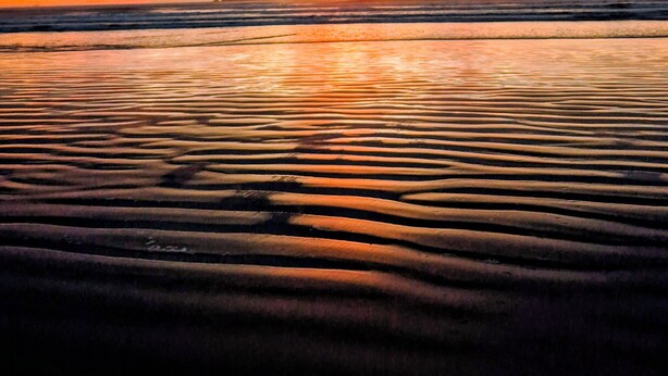 Een strand met zandrimpels en een zonsondergang.
