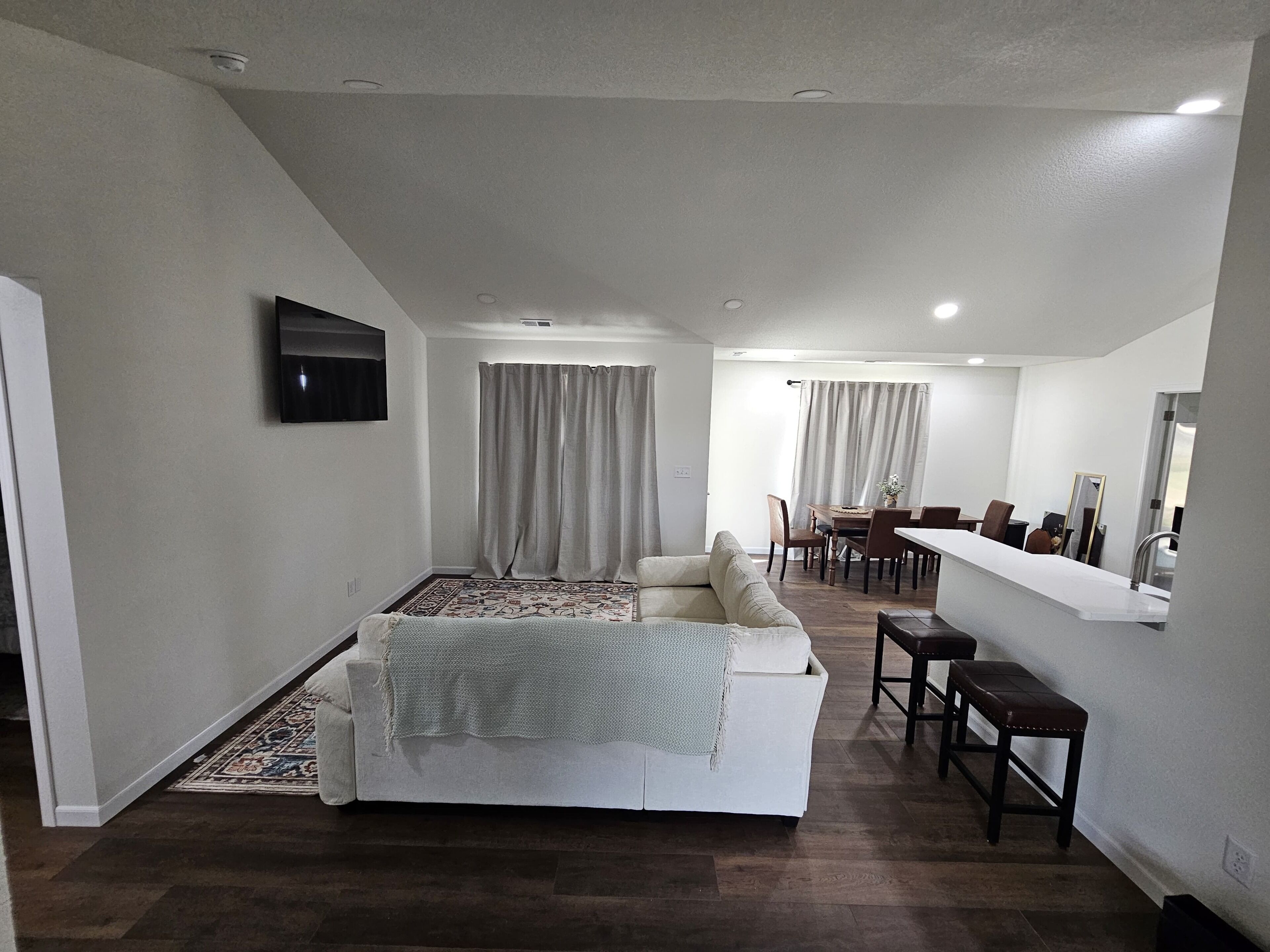 Un salon moderne comprenant un canapé, une table à manger et des chaises, un téléviseur à écran plat fixé au mur et un grand miroir.