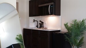 Una cocina compacta con armarios de madera oscura, un microondas integrado, un lavabo y un refrigerador pequeño.